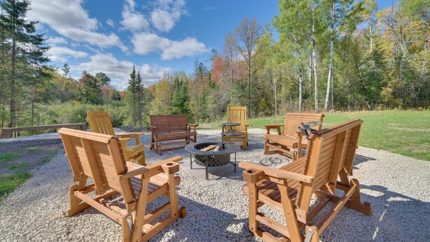 A fire pit surrounded by wooden chairs and a bench in a forested area. - UP Barndominium w/ Emus: Hike, Hunt & Fish (Rudyard)
