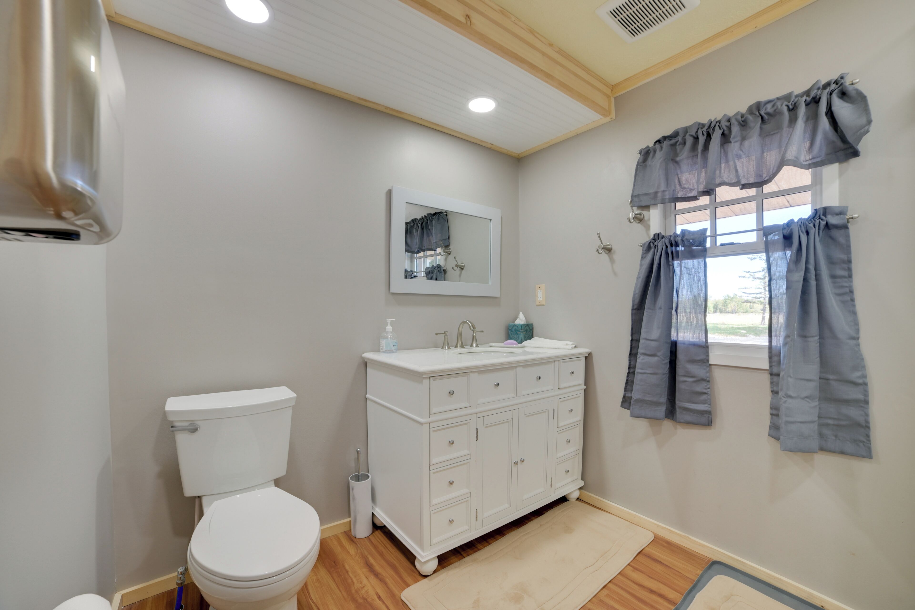 Een badkamer met toilet, wit wastafelmeubel, spiegel en raam met gordijnen.