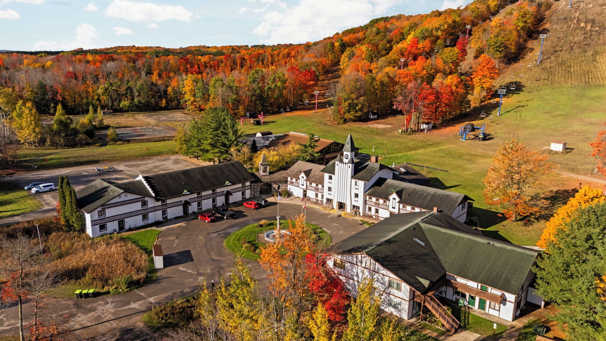 Ein Luftbild einer Lodge mit mehreren Gebäuden, einem Parkplatz und einem Hintergrund aus herbstlich gefärbten Bäumen.