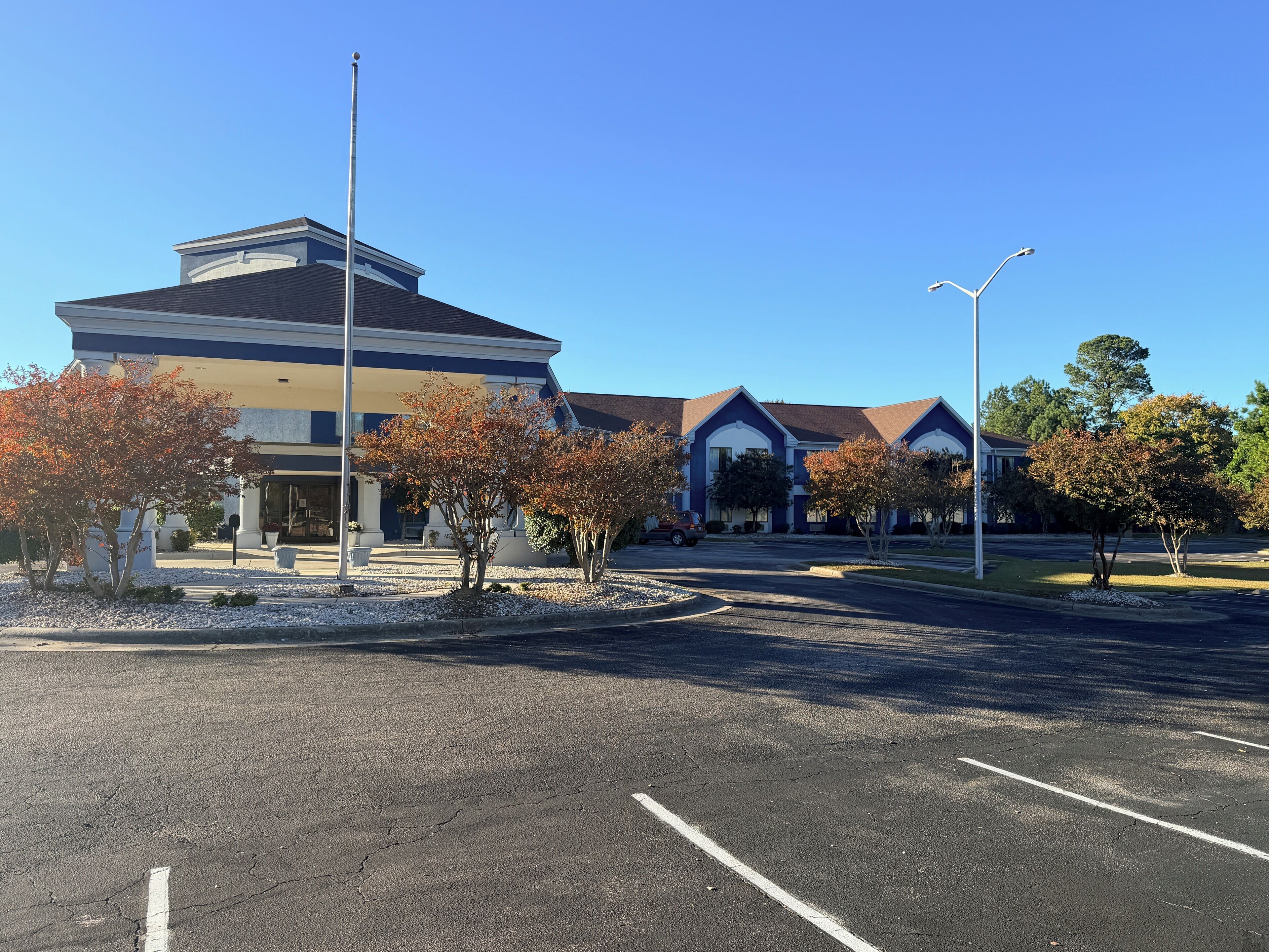 A building with a central entrance, parking lot, and surrounding trees.