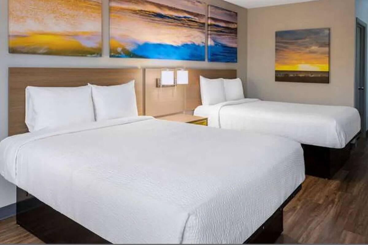 A hotel room with two beds, a wooden headboard, and three paintings on the wall.