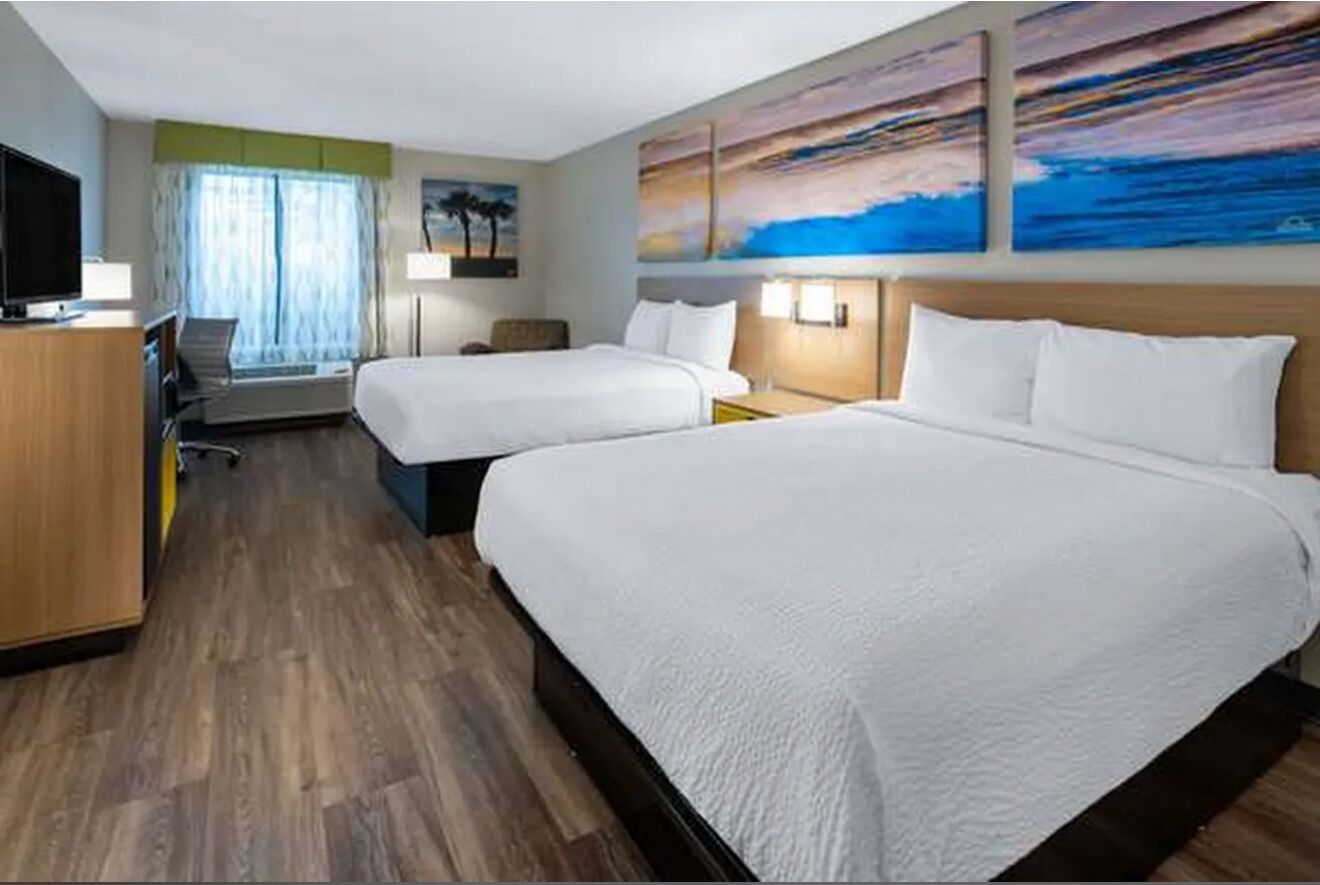 Ein Hotelzimmer mit zwei Betten, einem Schreibtisch, einem Fernseher und Bildern an den Wänden.