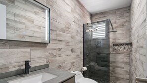 A modern bathroom with a wooden wall design, a glass shower enclosure, and a built-in sink. - Comfortable Home Prime PR Location 2-br Condo (Ceiba)