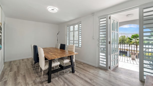 A dining area with a wooden table and chairs, a ceiling light, and a view of the outdoors through open doors. - Comfortable Home Prime PR Location 2-br Condo (Ceiba)