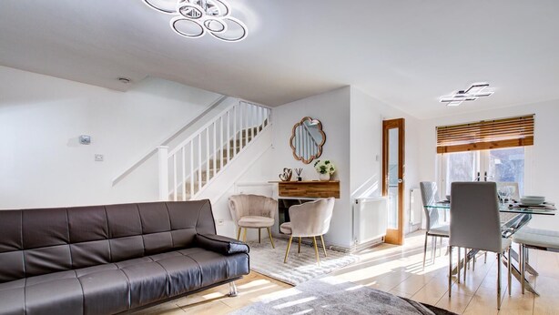 Una sala de estar moderna con un sofá de cuero, un comedor con una mesa de vidrio y una escalera.