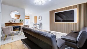 Una sala de estar moderna con sofá, sillas, televisor y zona de comedor.
