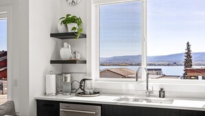 Eine moderne Küche mit einem großen Fenster, einer Kaffeemaschine, einem Wasserkocher und einer Pflanze auf einem Regal.