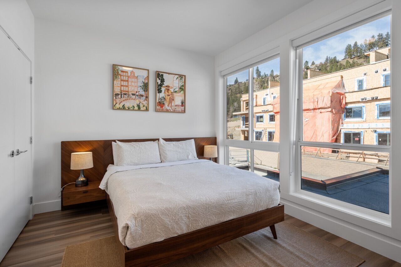 A bedroom with a large bed, two bedside tables, and a window with a view of buildings.