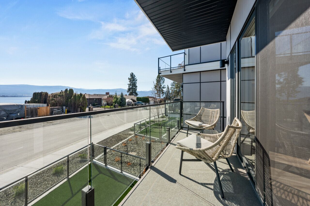 A modern building with a glass balcony overlooking a road and a body of water.