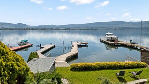 Ein See mit Ufergrundstück, einem Steg, einem Boot und einer Rasenfläche mit Stühlen.