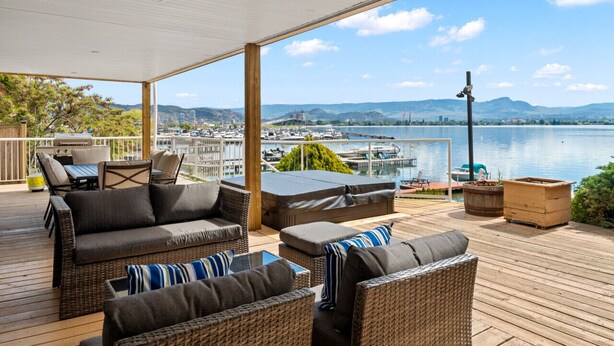 Eine überdachte Terrasse im Freien mit Korbmöbeln, Blick auf einen Hafen und einen See.