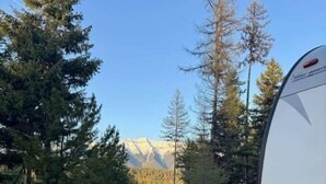 A white RV parked in a forested area with a mountain range in the background.