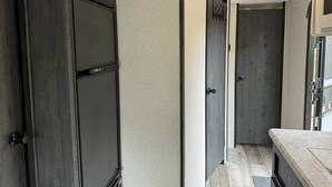 A narrow hallway with a dark door on the left, a light-colored wall, and a wooden counter on the right.