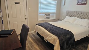 Une chambre à coucher comprenant un lit, un bureau, une chaise, une fenêtre avec des stores et un climatiseur fixé au mur.