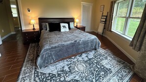 A bedroom with a large bed, two bedside tables with lamps, a ceiling fan, a window with curtains, and a view of the outdoors. - Casa Rotunda: A Cozy Catskills Escape (Margaretville)