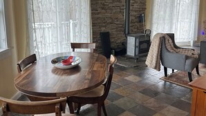 A dining area with a round wooden table, chairs, and a chandelier. There is a stone wall and a fireplace in the background. - Casa Rotunda: A Cozy Catskills Escape (Margaretville)