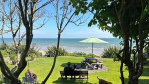 Un patio con vista sull'oceano, un ombrellone verde e un tavolo e una panca in legno.