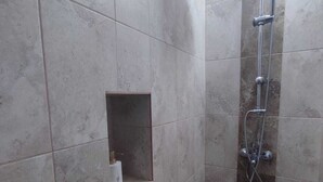 Une petite cabine de douche carrelée, équipée d’un pommeau de douche à main et d’un robinet fixé au mur.
