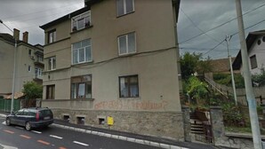 Un immeuble résidentiel à plusieurs étages, doté d’une façade plate, avec une voiture garée devant, et une rue dont les voies de circulation sont clairement délimitées.