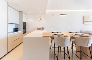 A modern kitchen with a central island, a dining area with four chairs, and a wall-mounted clock.
