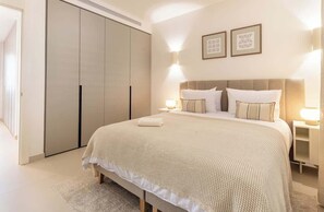 Een slaapkamer met een groot bed, bedlampen, een kledingkast en lijstjes met foto's aan de muur.