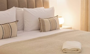 A neatly made bed with white linens and striped pillows, a folded towel, and a bedside lamp on a nightstand.