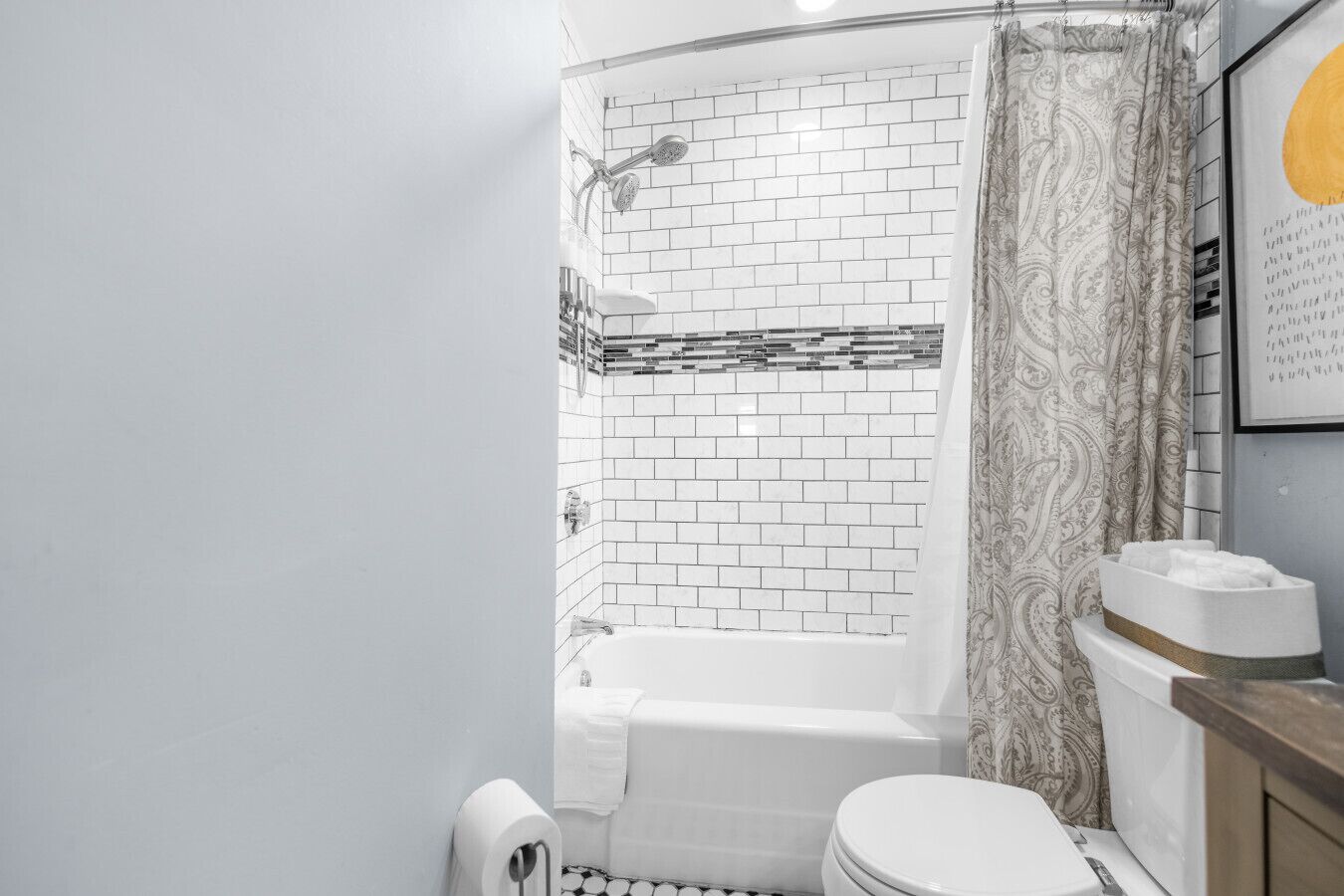 Um banheiro com banheira branca, vaso sanitário e chuveiro com cortina estampada.