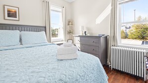 Ein Schlafzimmer mit Bett, Kommode, Heizkörper und einem Fenster mit Blick.