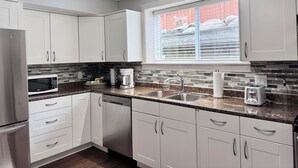 A modern kitchen with white cabinets, a stainless steel refrigerator, a microwave, a dishwasher, a coffee maker, and a toaster.