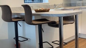 Moderni keittiö, jossa on pyöreä keittiösaareke, kaksi baarituolia, sinisillä verhoilla varustettu ikkuna ja pesuallas.