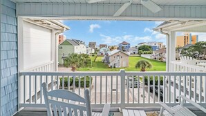 A covered porch with white railings and a ceiling fan, overlooking a residential area with houses and a well-maintained lawn. - Holly House / Poolside Getaway / Near the Beach (North Myrtle Beach)
