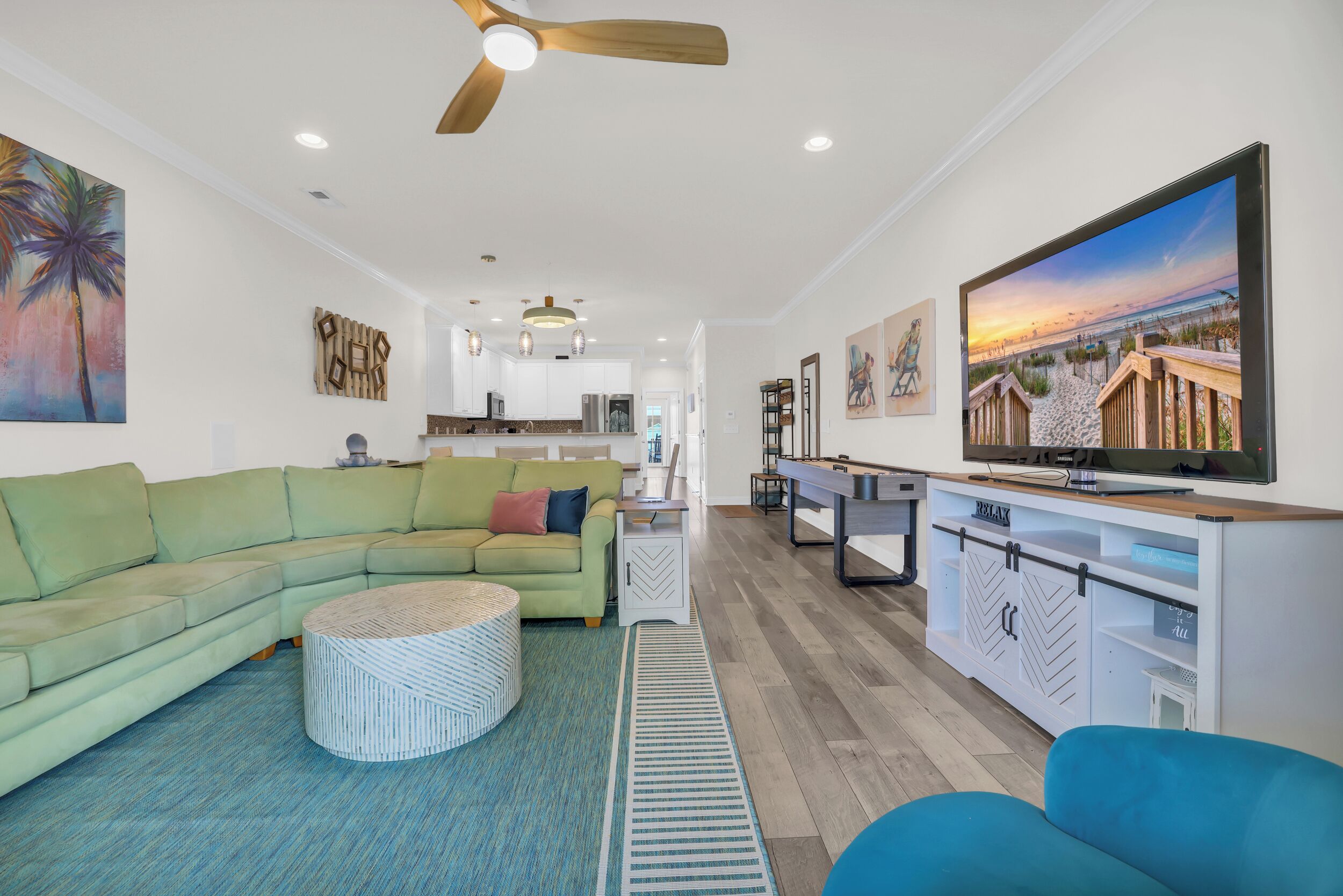 A modern living room with a sectional sofa, a round coffee table, a TV, and a kitchen in the background.