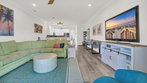 A modern living room with a sectional sofa, a round coffee table, a TV, and a kitchen in the background. - Holly House / Poolside Getaway / Near the Beach (North Myrtle Beach)