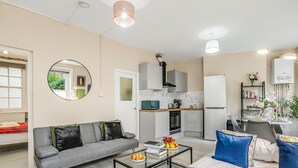 Una sala de estar moderna con un sofá, una mesa de centro y una cama. Hay una zona de cocina con refrigerador, microondas y estufa.