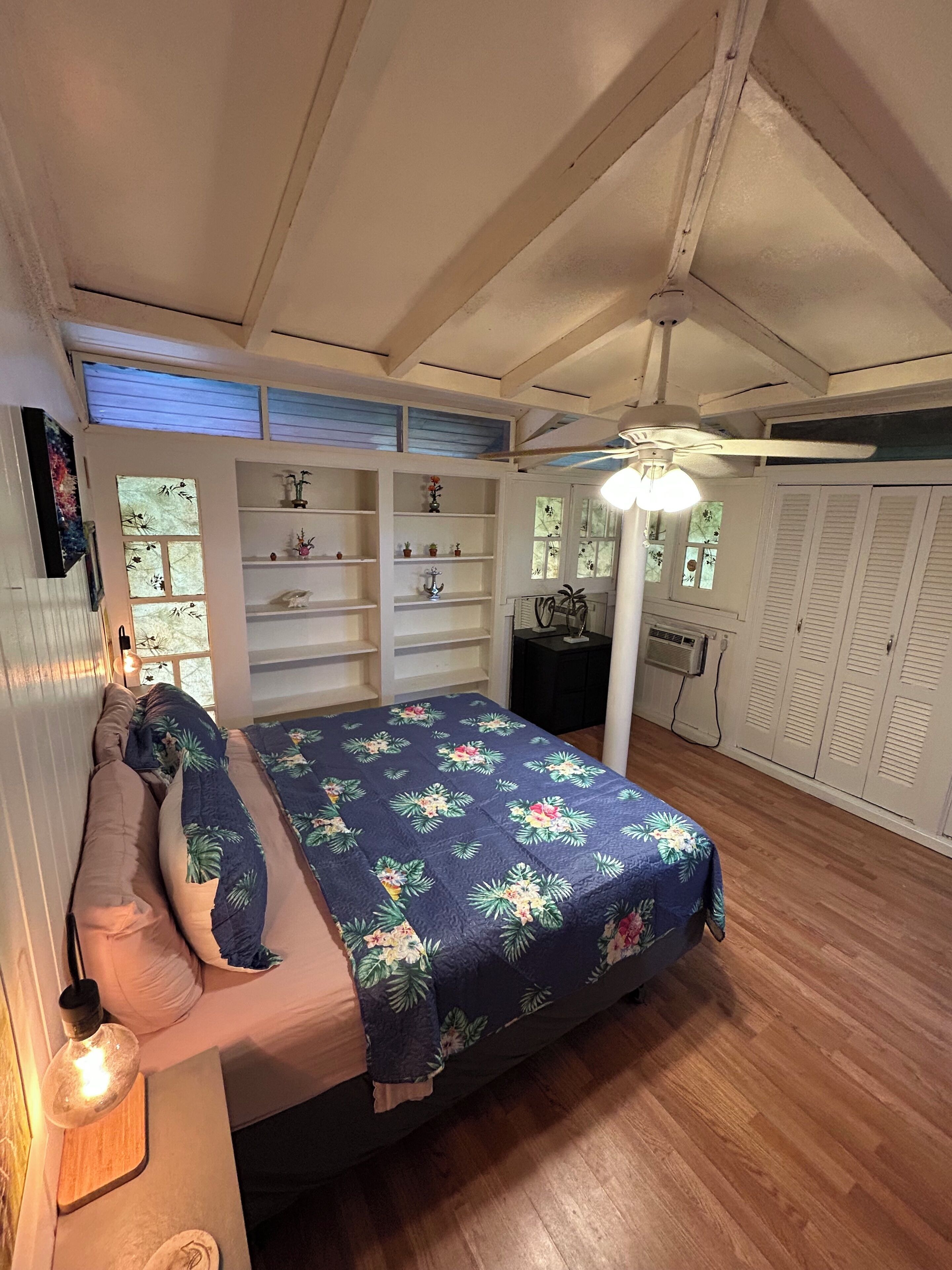 A bedroom with a bed, bedside tables, a ceiling fan, and a window with shutters.