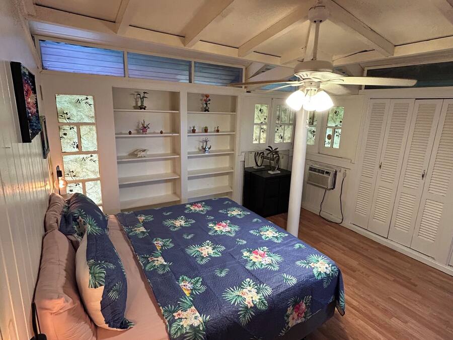 A bedroom with a bed, bedside tables, a ceiling fan, and a window with shutters.