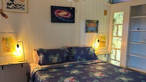 A bedroom with a large bed, wooden flooring, a ceiling fan, and wall-mounted artwork. - Shibui Cove (St. Thomas)