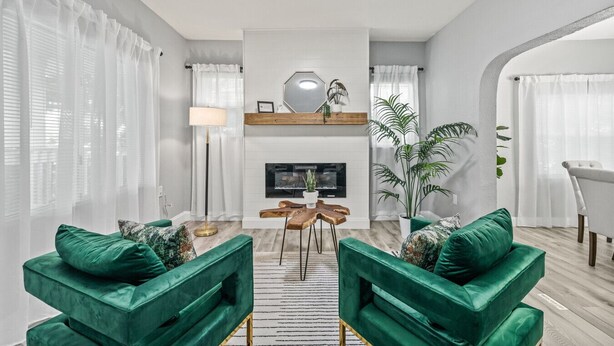 Una sala de estar moderna con chimenea, sofás verdes, una mesa de centro y un comedor con mesa y sillas de madera.