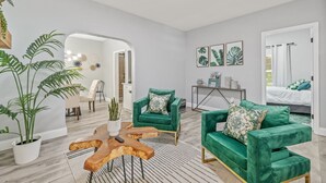 Amplia sala de estar con dos sofás de terciopelo verde, una mesa de centro de madera y un comedor con mesa y sillas blancas.