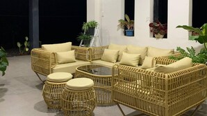 Uma área de estar coberta ao ar livre, com mobiliário de vime e plantas em vasos.