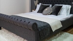 A modern bedroom with a tufted headboard, a bed with multiple pillows, a white rug, and an air conditioning unit mounted on the wall. - Experience the ultimate relaxation and privacy in Gray's Farmhouse. (Quezon)