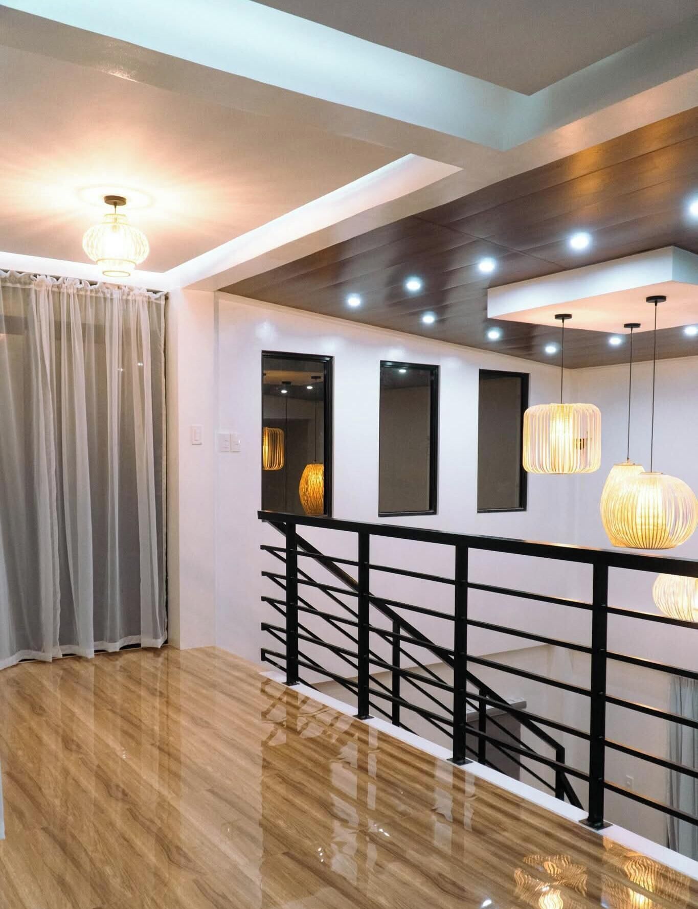Un interior moderno con suelo de madera, una escalera con barandillas negras e iluminación colgante.