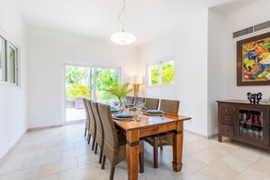 Un coin repas avec une table en bois dressée pour six personnes, entourée de chaises en osier. On peut voir une plante en pot sur la table et, à droite, un meuble avec des portes en verre.