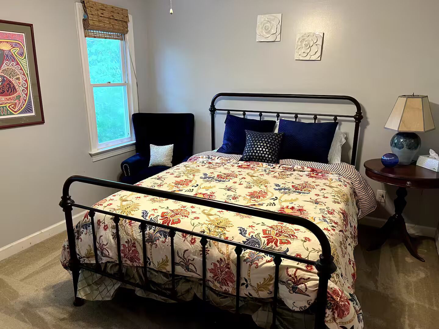 A bedroom with a metal bed frame, floral bedspread, and a window with a view.