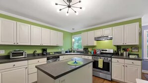 A kitchen with white cabinets, a central island, a stove, and a coffee maker. - Cary garden home close to SAS, RDU & RTP (Cary)