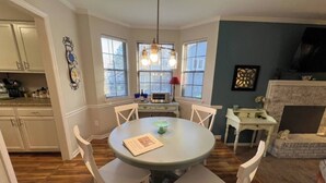 A dining area with a round table, four chairs, a chandelier, and a fireplace.