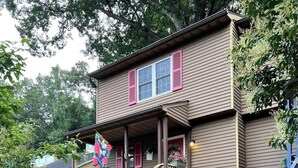 A two-story house with a wooden staircase, a porch with red shutters, and a garden area with a birdbath.