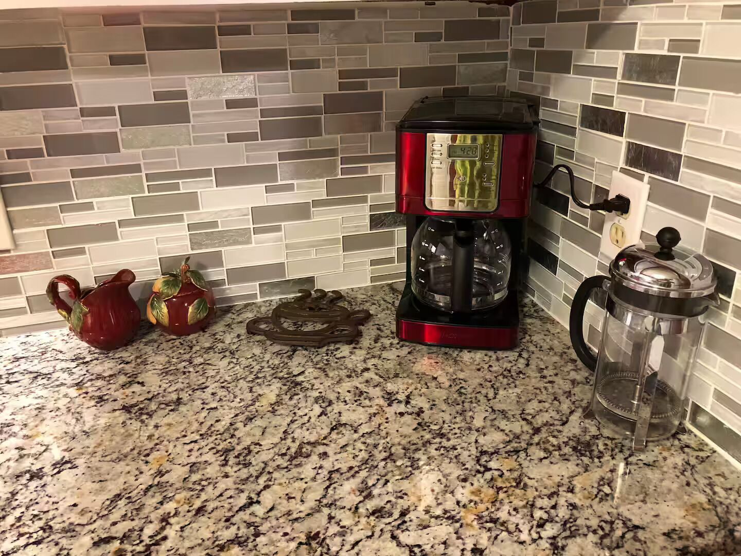 Une cuisine équipée d’une machine à café, d’une cafetière à piston et de deux théières décoratives posées sur un plan de travail en granit.