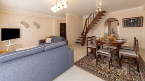 Een woonkamer met een bank, televisie en een eethoek met een tafel en stoelen.
