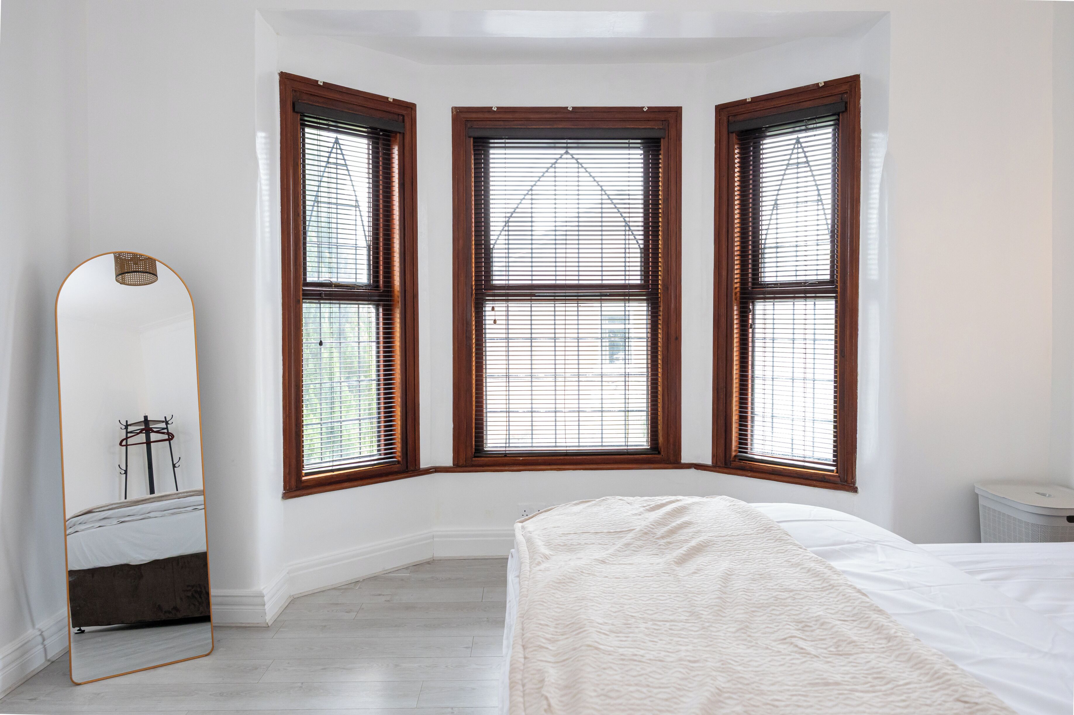 Une chambre avec un grand lit, un miroir en pied et trois fenêtres à cadres en bois.